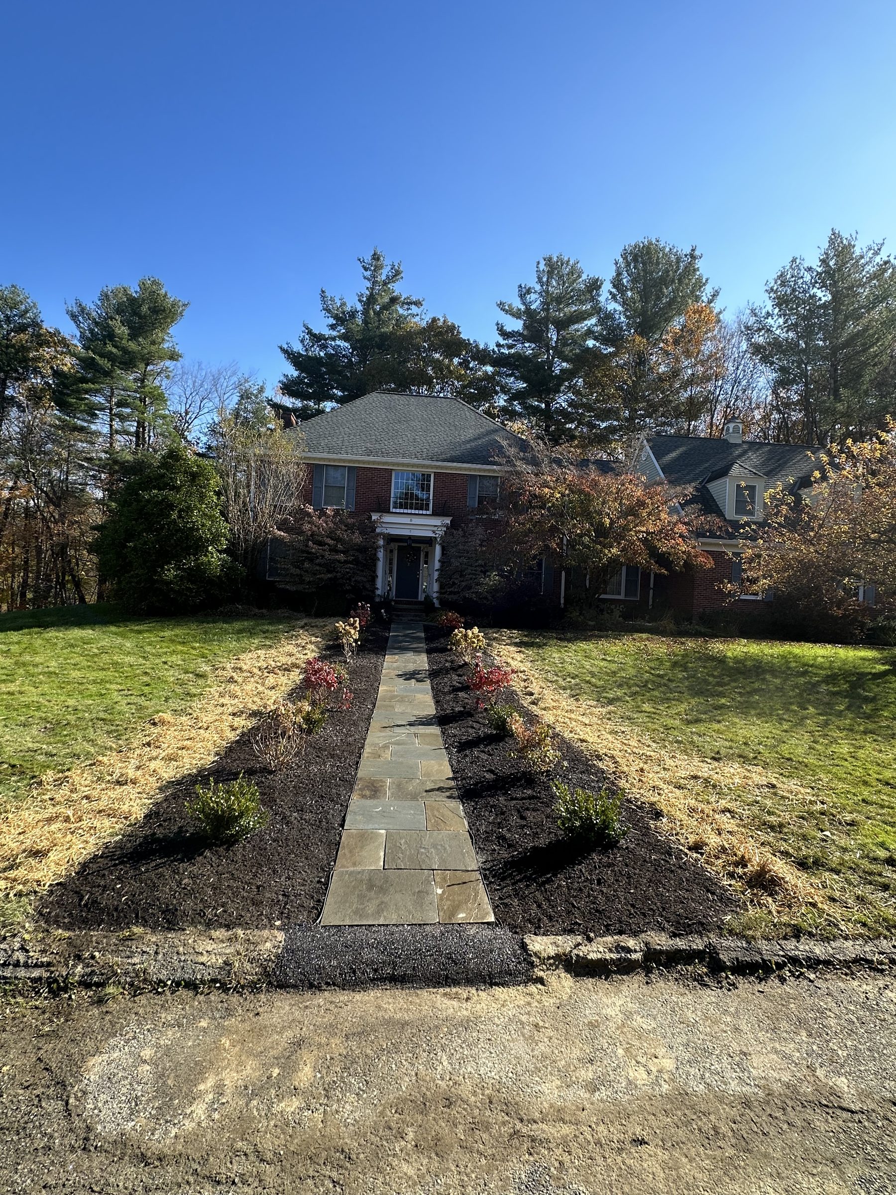Stone walkway leading up a lawn to a brick colonial home