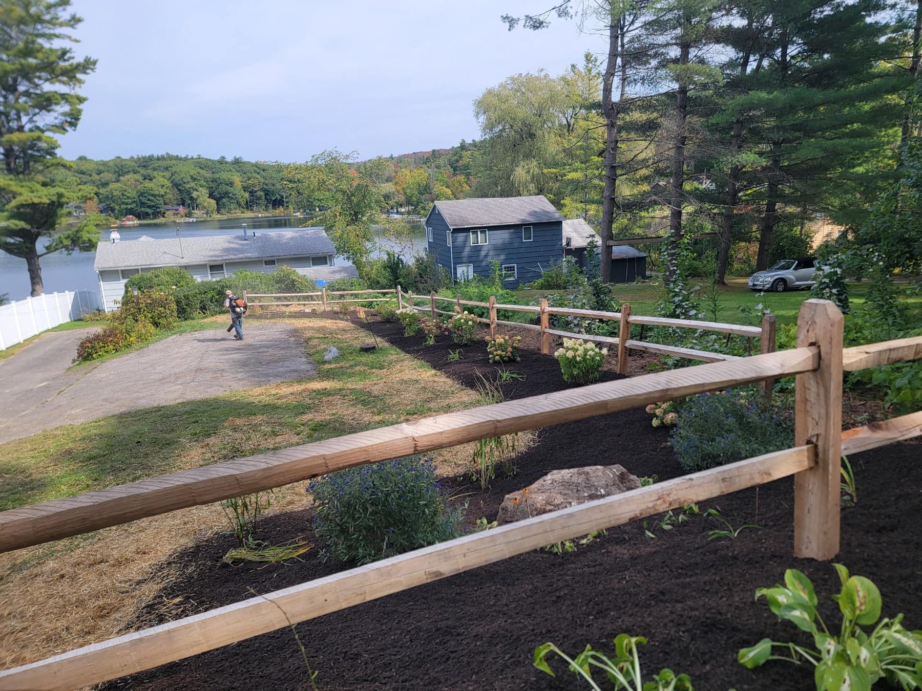 Hillside plantings with a split rail fence above the water